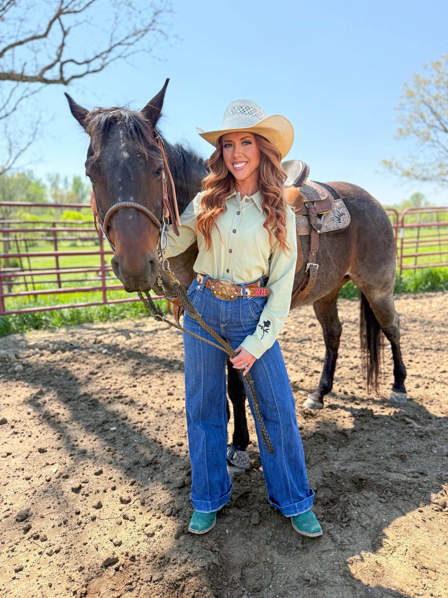 Woman in cowboy hat and jeans standing next to a horse in an outdoor setting