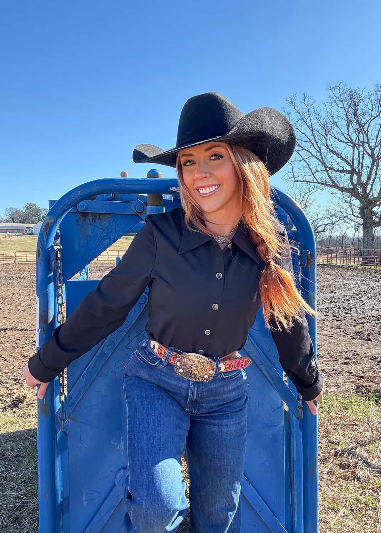 Woman in cowboy hat and black shirt standing in a blue gate outdoors.