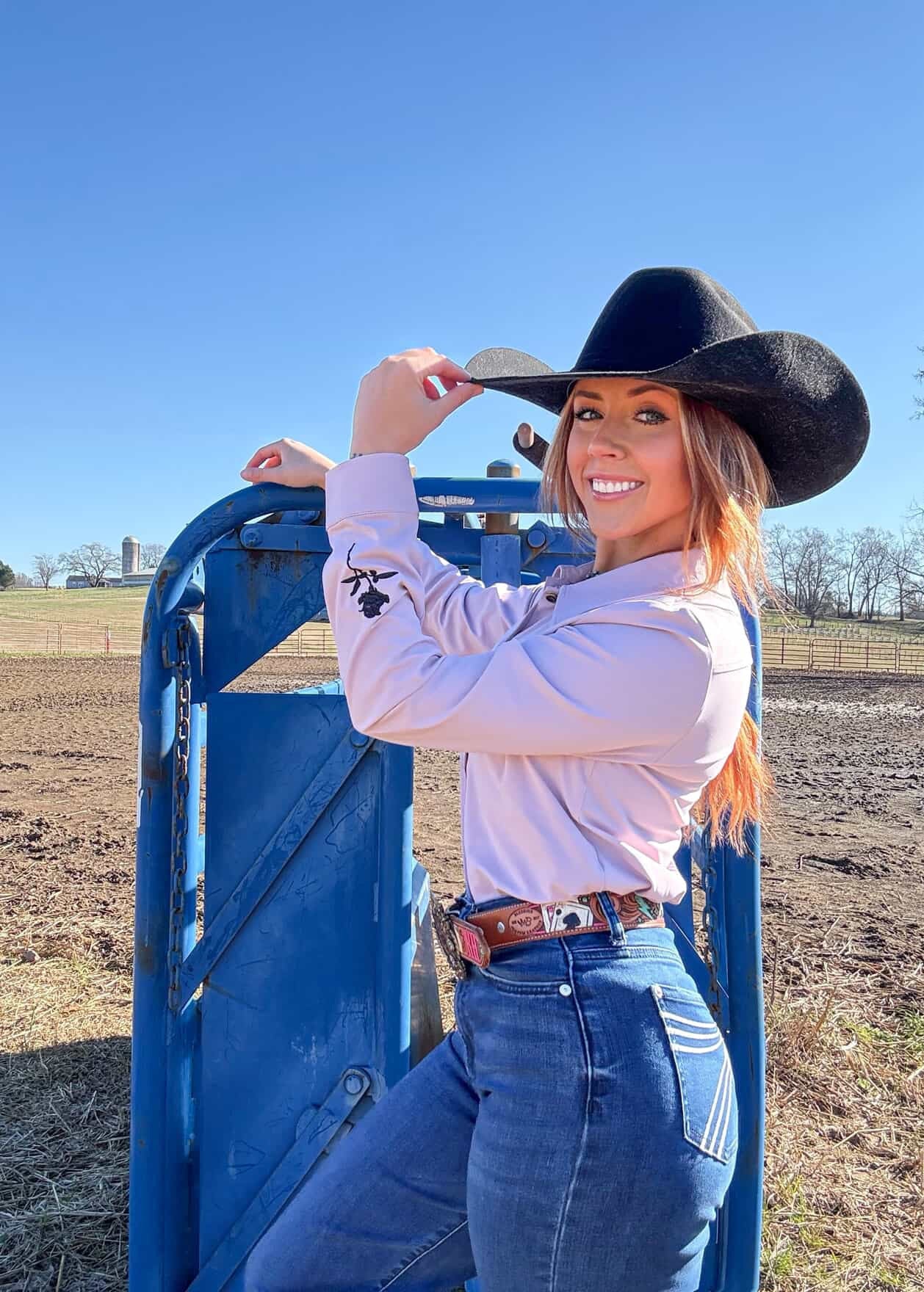 Woman in cowboy hat and shirt standing next to a blue gate in an open field.