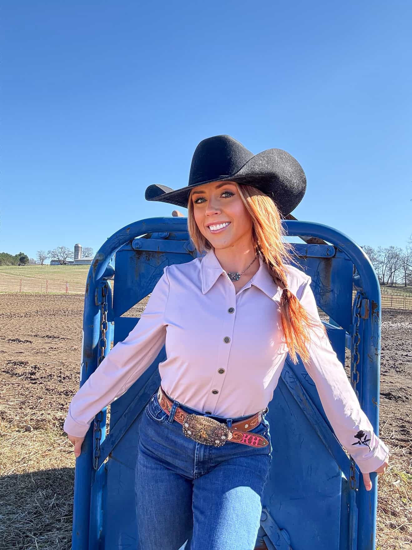 Woman in cowboy hat and western attire standing in a field with blue sky.