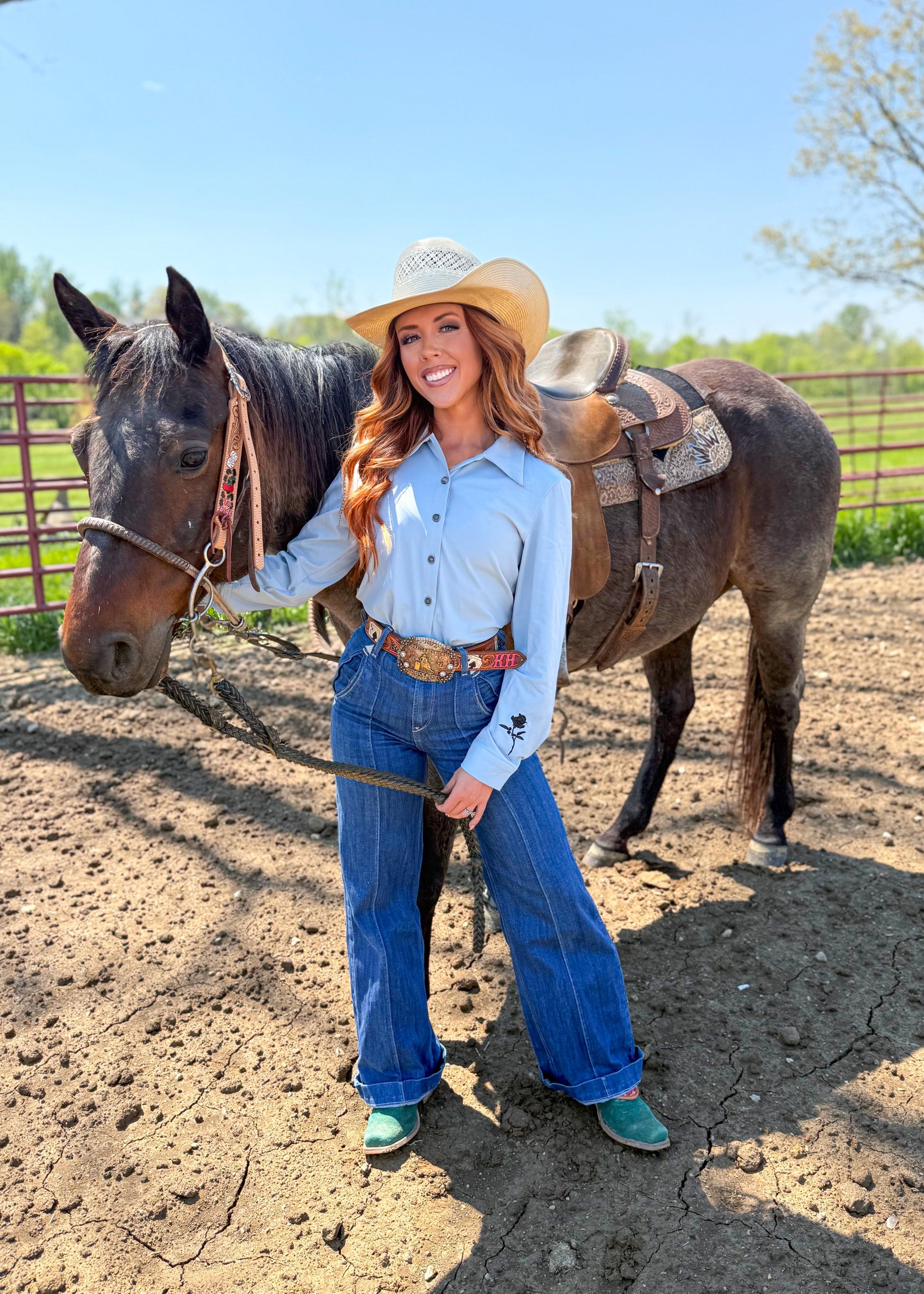 Woman in cowboy hat and blue jeans standing next to a horse in an outdoor setting