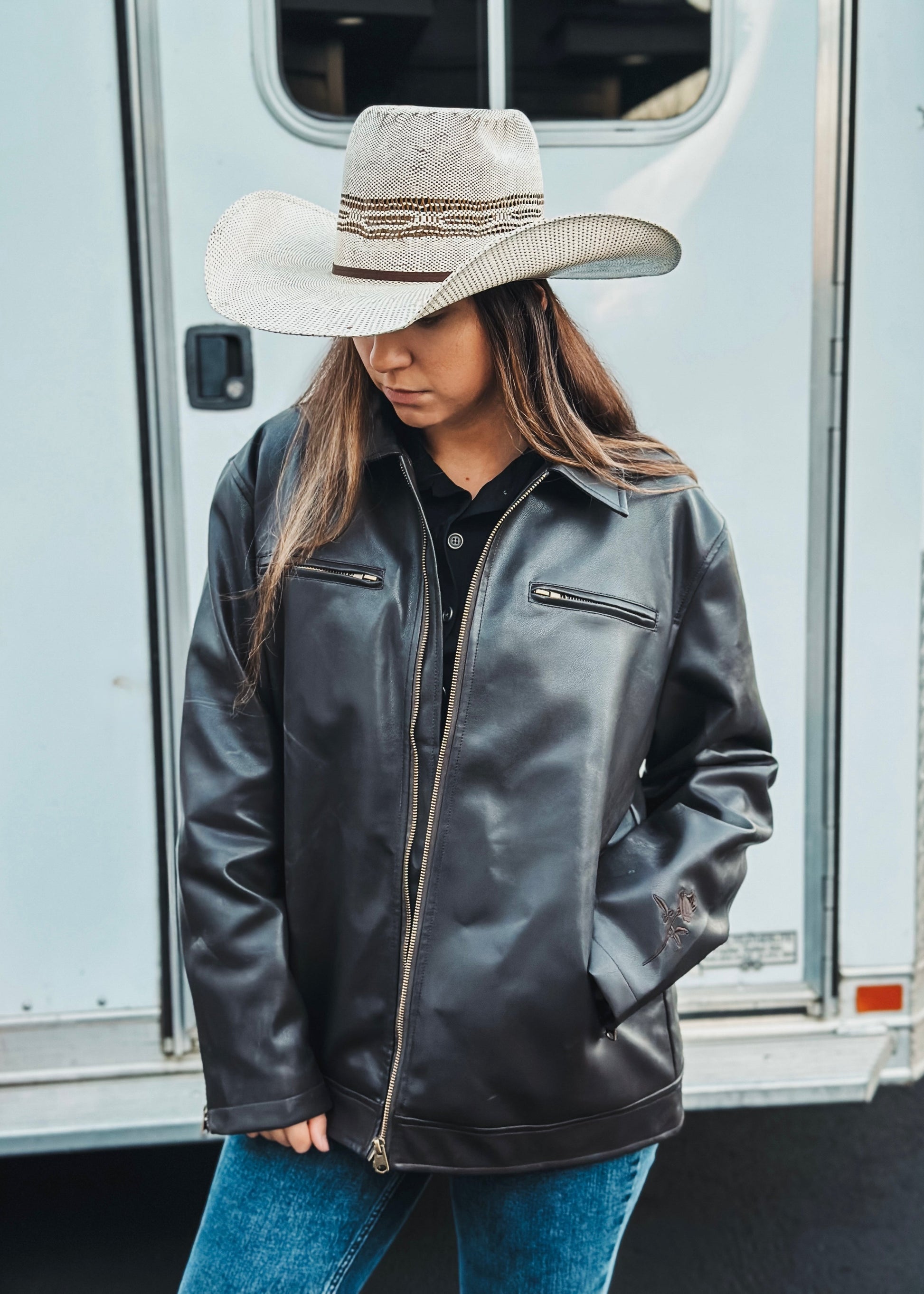 Person wearing a black leather jacket and white cowboy hat in front of a trailer.
